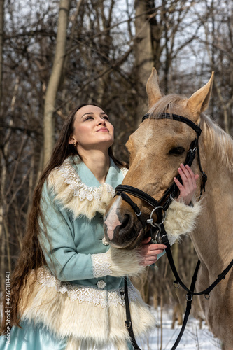 beautiful woman in blue suit with light brown horse in spring forest 