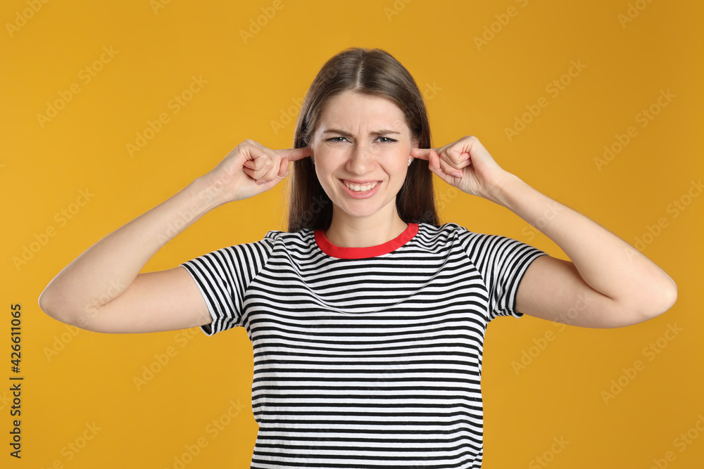 Emotional young woman covering her ears with fingers on yellow background Emotional young woman covering her ears with fingers on yellow background