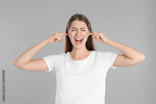 Emotional young woman covering her ears with fingers on grey background