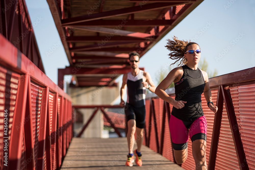 Young triathletes run down a path outdoors giving one last effort to reach their destination Young triathletes run down a path outdoors giving one last effort to reach their destination