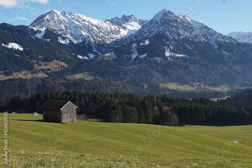 Winteruntypisches Bergpanorama in den Allgäuer Alpen mit grünen Talflanken und Schnee nur auf den Gipfeln