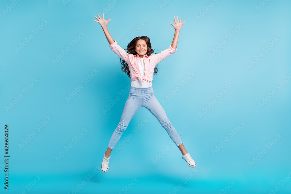 Full body portrait of carefree school girl jumping raise hands have fun isolated on blue color background