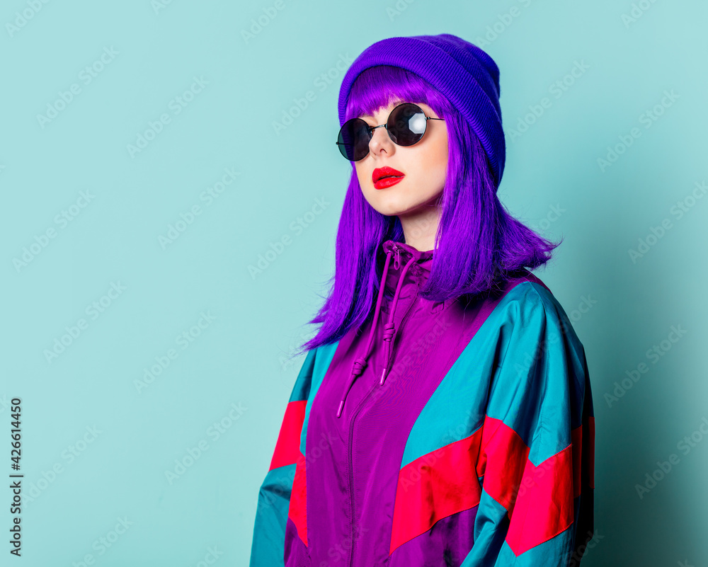 Stylish white girl with purple hair, 80s tracksuit and sunglasses on blue background