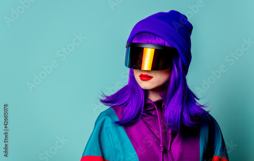 Stylish girl in cyber punk glasses and 80s tracksuit on blue background © Masson