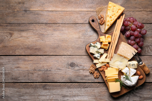 Cheese plate with grapes and nuts on wooden table, top view. Space for text