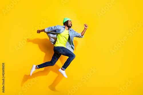 Full size profile side photo of brunette dark skin man jump up run empty space sale isolated on yellow color background