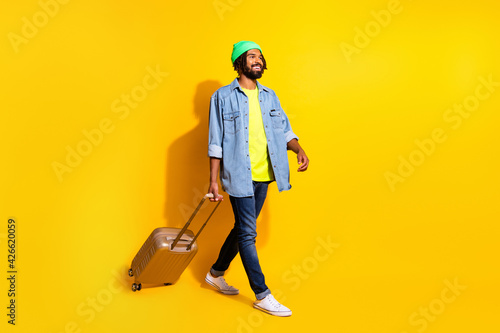 Full size profile side photo of young happy cheerful afro man look copyspace go with baggage isolated on yellow color background