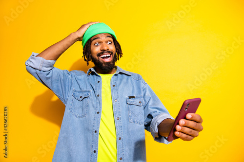 Photo of young happy smiling cheerful shocked amazed man winning on online victory isolated on yellow color background