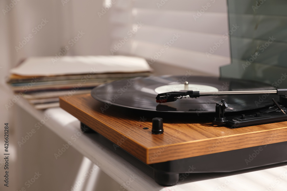 Stylish turntable with vinyl disc on windowsill in room, closeup