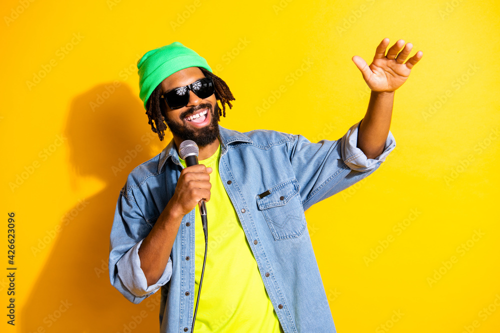 Photo of young cheerful smiling good mood african man in sunglasses singing in karaoke isolated on yellow color background
