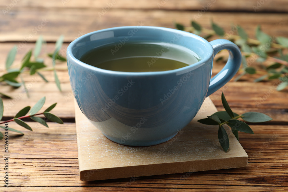 Cup of green tea and eucalyptus leaves on wooden table Cup of green tea and eucalyptus leaves on wooden table