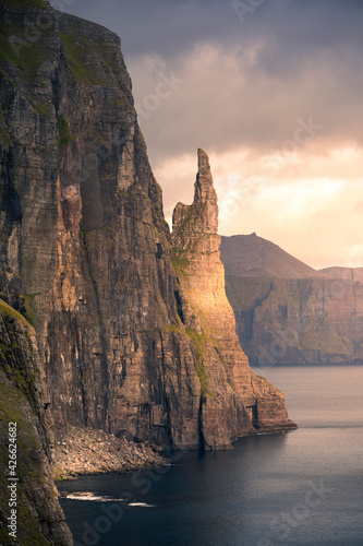 The rock formation in the shape of a witch's finger is called Trøllkonufingur. It is located on the coast of the island of Vagar. The last rays of the sun hit the rock at sunset..