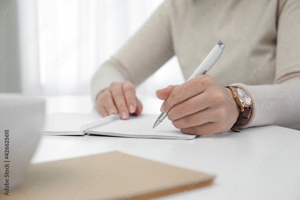 Left-handed woman writing in notebook at table indoors, closeup. Space for text Left-handed woman writing in notebook at table indoors, closeup. Space for text