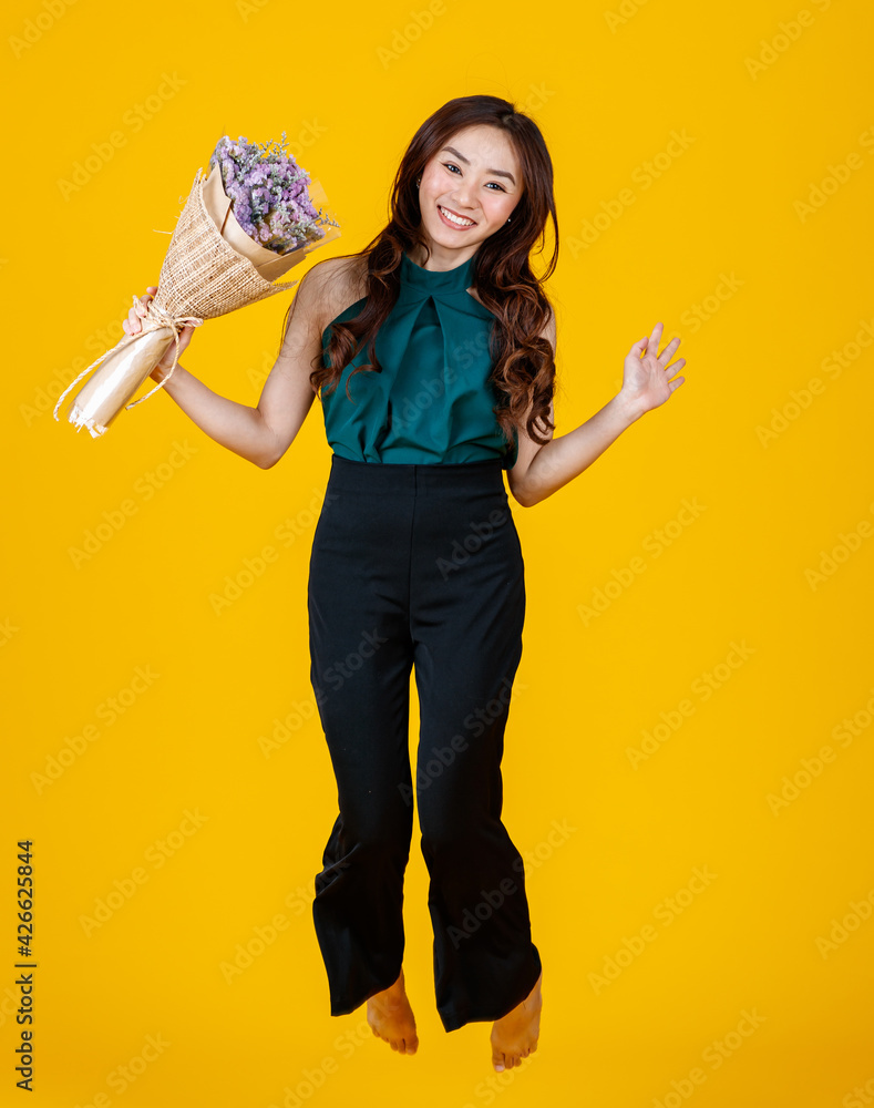 Excited in love Asian female brunette holding a flower bouquet high jumps into the air with cheerful and very happy. Freeze stop action with studio shot isolated on bright yellow background. Excited in love Asian female brunette holding a flower bouquet high jumps into the air with cheerful and very happy. Freeze stop action with studio shot isolated on bright yellow background.