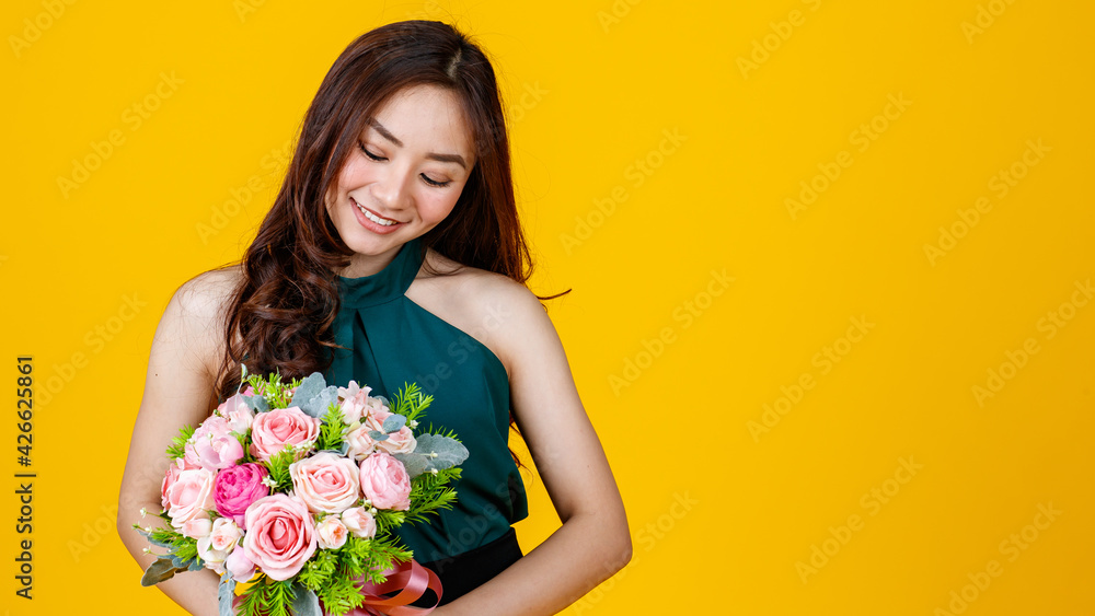 Young cute and pretty curly hair Asian female brunette holding flower bouquet with cheerful and happy, studio shot isolated on bright yellow background.
