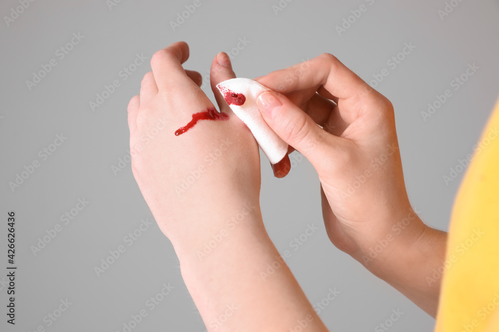 Woman wiping cut finger with cotton pad on grey background, closeup Woman wiping cut finger with cotton pad on grey background, closeup