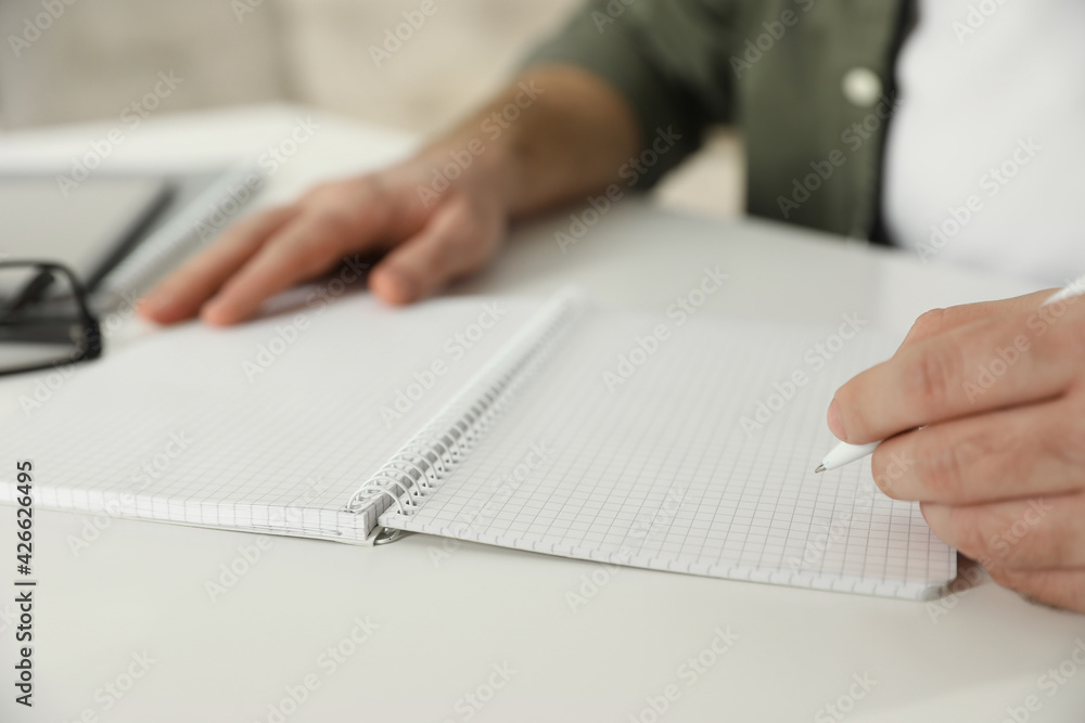 Fototapeta premium Left-handed man writing in notebook at white table, closeup