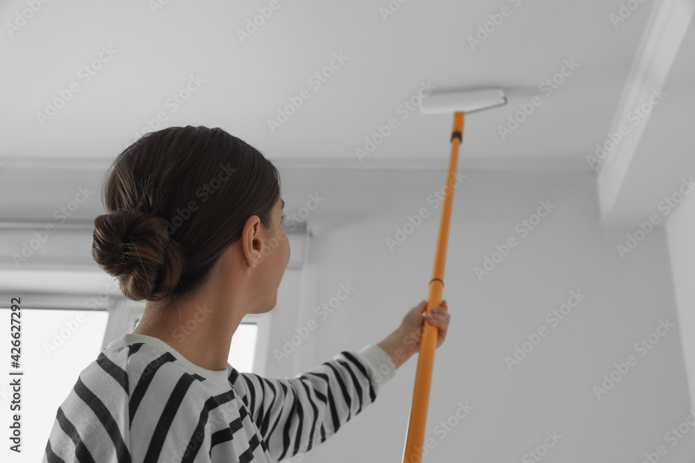 Young woman painting ceiling with white dye indoors, back view Young woman painting ceiling with white dye indoors, back view