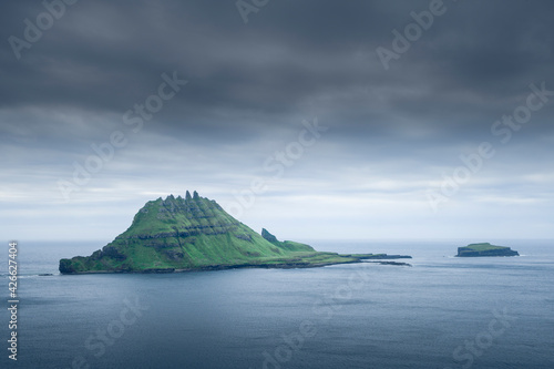 Rocky green island of Tindholmur, in the sea under dark clouds, Faroe Islands.