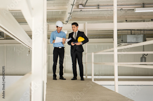 Wallpaper Mural Asian businessman boss wearing black suit standing and discussing with young engineer in construction site. Concept for brainstorming, review, and inspecting work results Torontodigital.ca