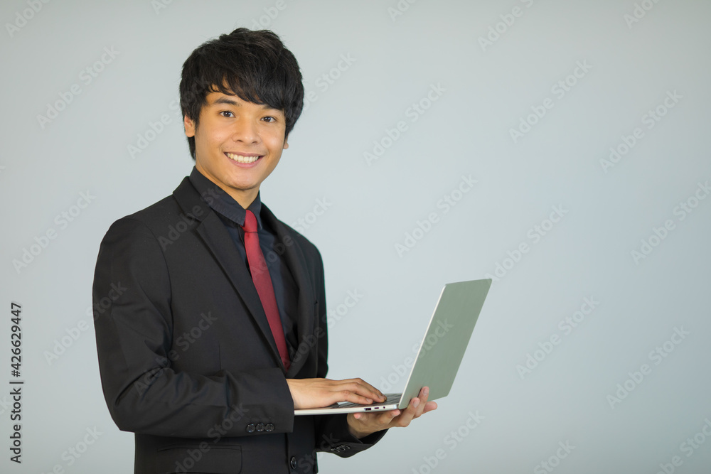 Cute and handsome Asian businessman executive look in formal suit standing and holding laptop notebook computer Cute and handsome Asian businessman executive look in formal suit standing and holding laptop notebook computer
