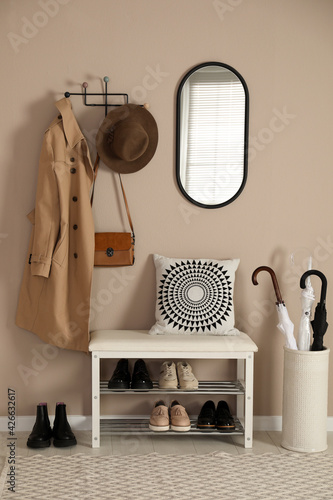 Stylish storage bench with different pairs of shoes near beige wall in hall © New Africa