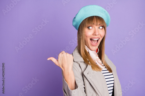 Photo of excited girl indicate thumb empty space open mouth wear blue beret coat isolated purple color background © deagreez