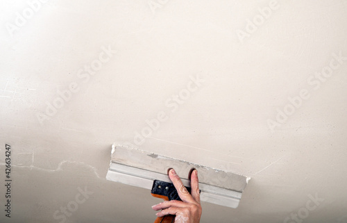 Hand of builder worker spacks ceiling with putty plaster aligning ceiling with spatula. Renovation and construction works photo