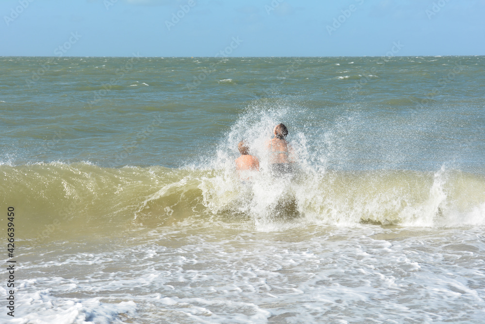 Two children in the middle of a breaking wave with blue sky