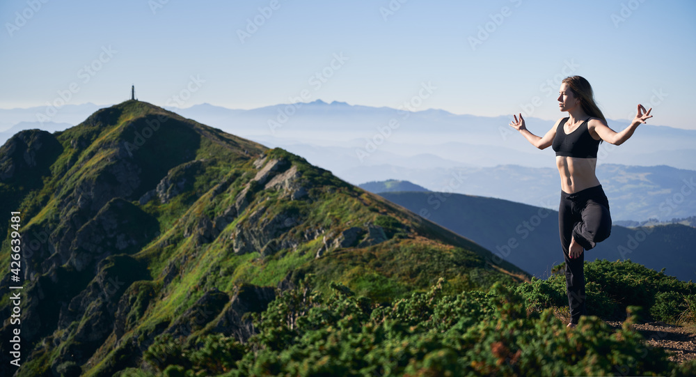 Young slim woman in black sportswear doing meditating on incredible nature background. Concept of yoga time in mountains with beautiful views.