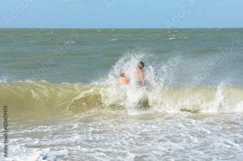 Two children in the middle of a breaking wave with blue sky