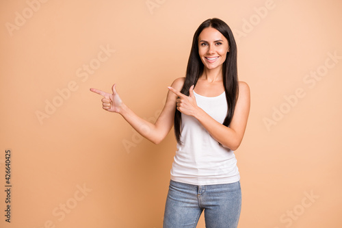 Photo portrait of girl pointing two fingers at blank space isolated on pastel beige colored background