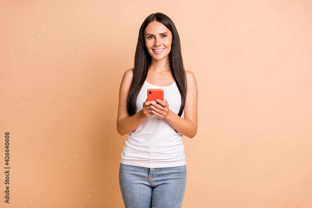 Photo of optimistic brunette girl hold telephone wear white top jeans isolated on pastel beige color background Photo of optimistic brunette girl hold telephone wear white top jeans isolated on pastel beige color background