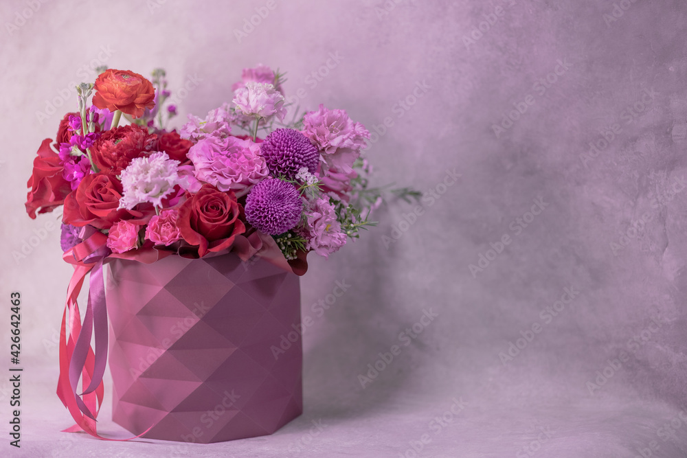 A lush bouquet of red, purple, light pink, white cute delicate small roses of different sizes, flowers in round paper box with geometric pattern. Romance. Place for text