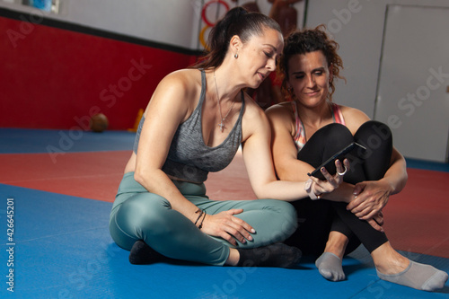 two women seated on the gym floor looking at a smartphone