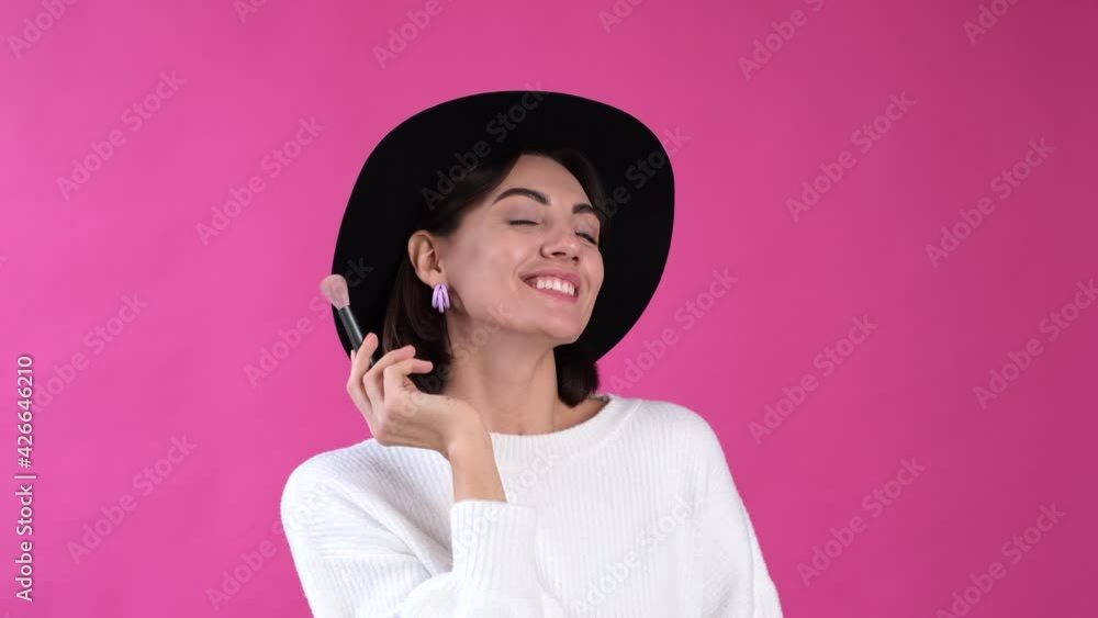 Woman in casual white sweater and hat on pink background isolated happy put blush using brush smile Woman in casual white sweater and hat on pink background isolated happy put blush using brush smile