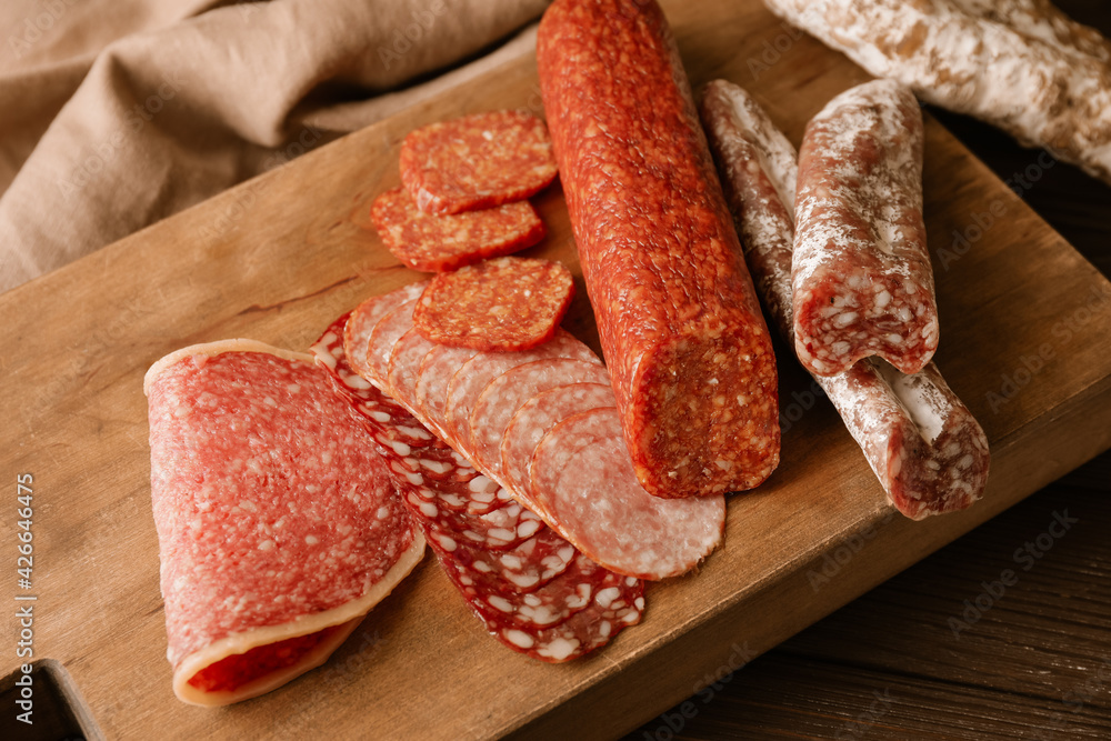 Cutting board with tasty sausages on wooden background Cutting board with tasty sausages on wooden background