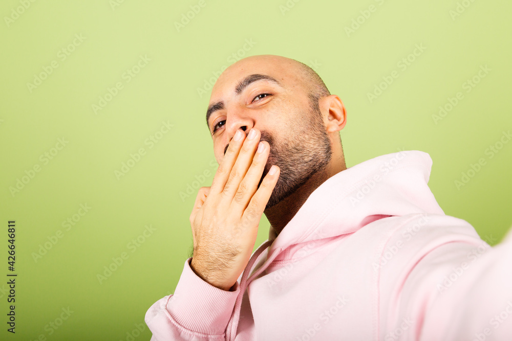 Young bald caucasian man in pink hoodie isolated on green background positive cheerful take photo selfie Young bald caucasian man in pink hoodie isolated on green background positive cheerful take photo selfie