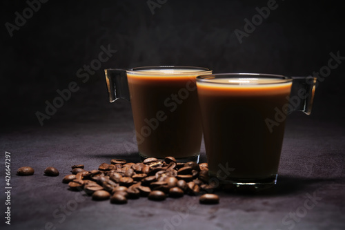 two cups of coffee with milk and scattered coffee beans