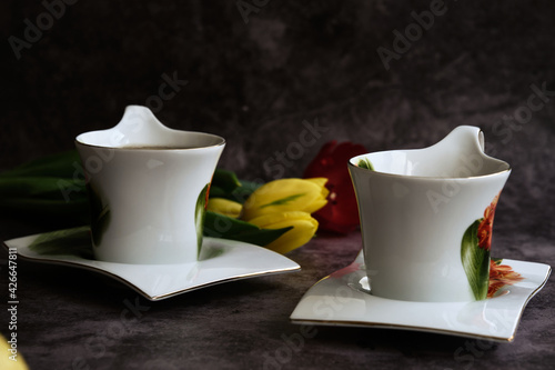 two white cups of tea and yellow and red tulips