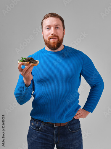 young man with a sandwich with wild black beluga caviar on a light uniform background