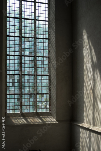 Church stained-glass window with sunlight shining through. The incoming light shines on the wall next to the window