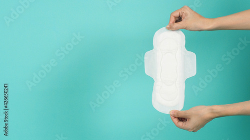 Hand is holding Sanitary napkin soft wings use on mint or green or Tiffany Blue background.