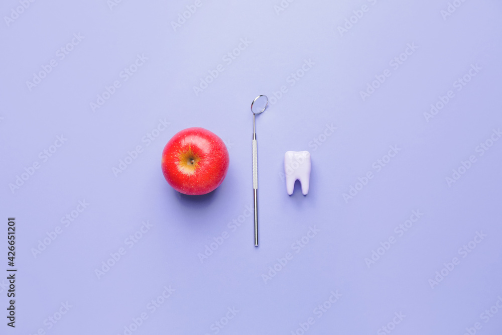 Dentist's mirror, plastic tooth and apple on color background Dentist's mirror, plastic tooth and apple on color background