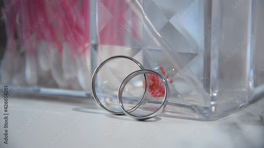Close-up of wedding rings. wedding rings stand on a white table on a glass background, and then fall, silver wedding rings, Rings lie on the table and sparkle in the rays of soft light Close-up of wedding rings. wedding rings stand on a white table on a glass background, and then fall, silver wedding rings, Rings lie on the table and sparkle in the rays of soft light