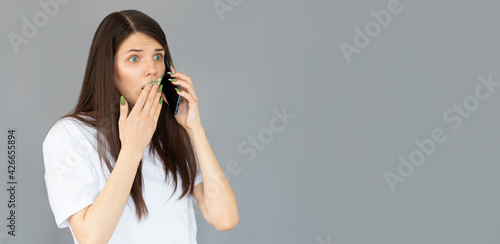 Headshot of shocked woman having argument talking via smartphone. Angry young female speak irritated by cell phone, hear bad news using phone. Portrait of girl with mobile isolated on gray © Яна Солодкая