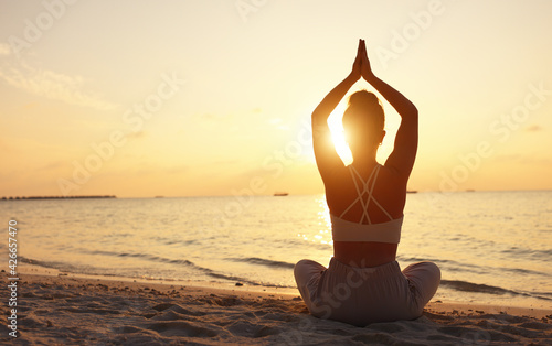 Calm woman meditating on beach at sunset