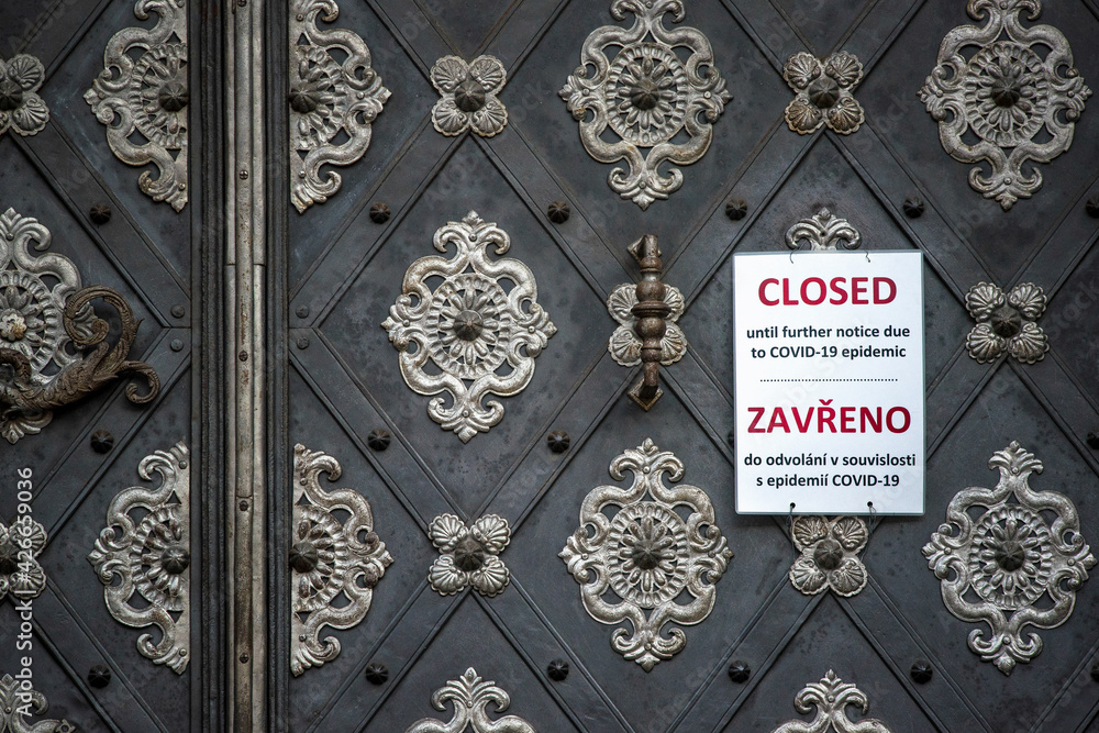 Closed until further notice due to Covid-19 epidemic. This text in English and Czech languages on white sign hanging on ancient metal door gate of UNESCO protected Prague Castle Complex. Detail.