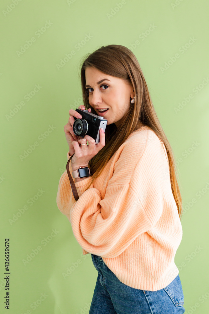 Pretty european woman in casual peach sweater isolated on green background with camera in hands positive smile happy Pretty european woman in casual peach sweater isolated on green background with camera in hands positive smile happy