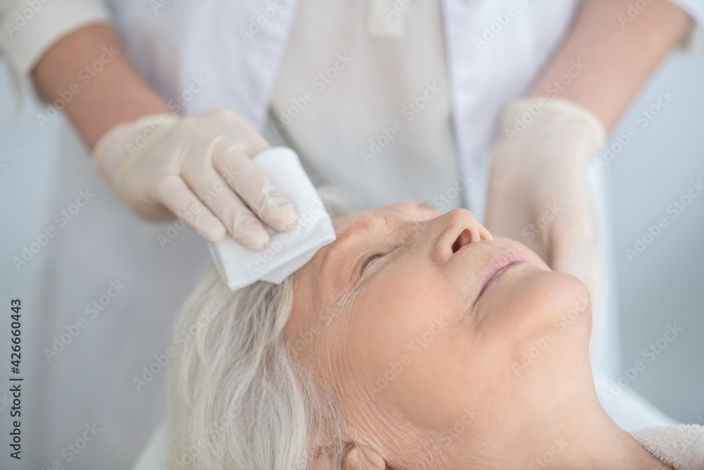 Cosmetologist wiping the customers face with a napkin Cosmetologist wiping the customers face with a napkin